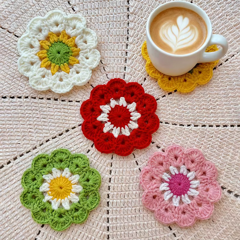 Rust and deep red crochet flower coaster with green leaf details on a warm beige background